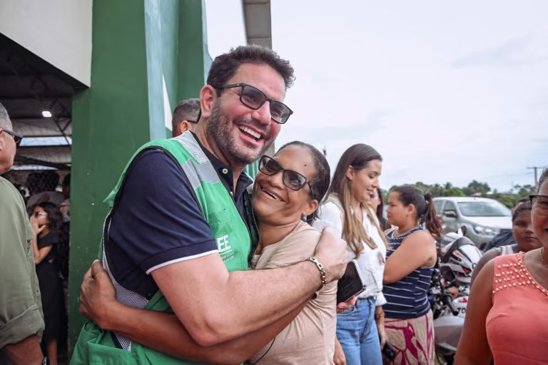 Gladson Cameli abraça uma moradora sorridente em um evento ao ar livre