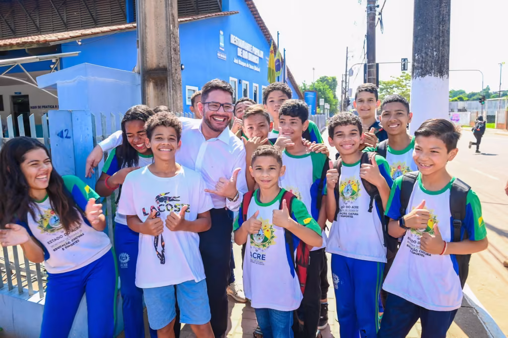 Gladson Cameli com estudantes de uniforme escolar em frente a uma escola